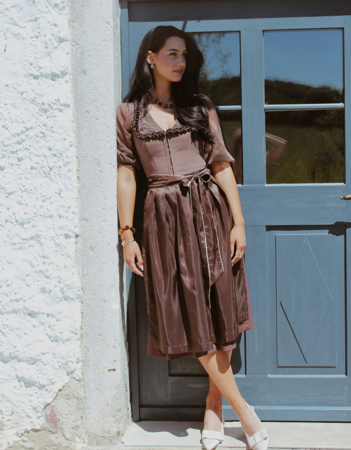 Model trägt Dirndl Haselnuss in Braun vor rustikaler Kulisse