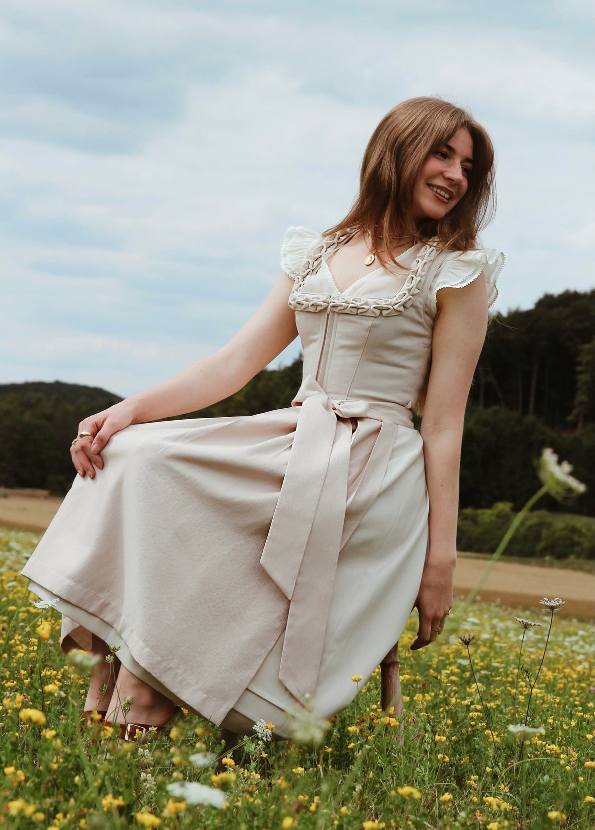 Model trägt Dirndl Soft Pearl in Beige auf einer Blumenwiese